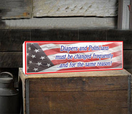 Humorous novelty sign featuring the quote 'Diapers and Politicians Must Be Changed Frequently and For the Same Reason' on a waving flag background