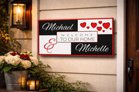 Welcome to Our Home couple sign mounted on an exterior house wall near a front porch with warm lighting and flowers
