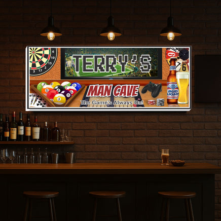personalized man cave wall sign hanging above a bar shelf, featuring sports graphics, pool balls, darts, beer glass, and video game controller, custom name in the center