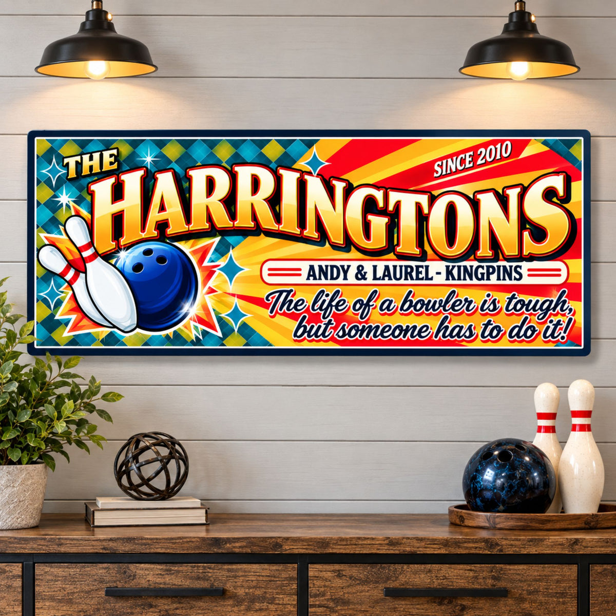 Personalized family bowling sign mounted on a wall beneath pendant lights with bowling equipment below.