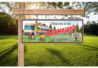 Personalized RV camping welcome sign featuring distant pine trees, a crackling campfire surrounded by wooden chairs, and a custom name. All lines of text are editable.