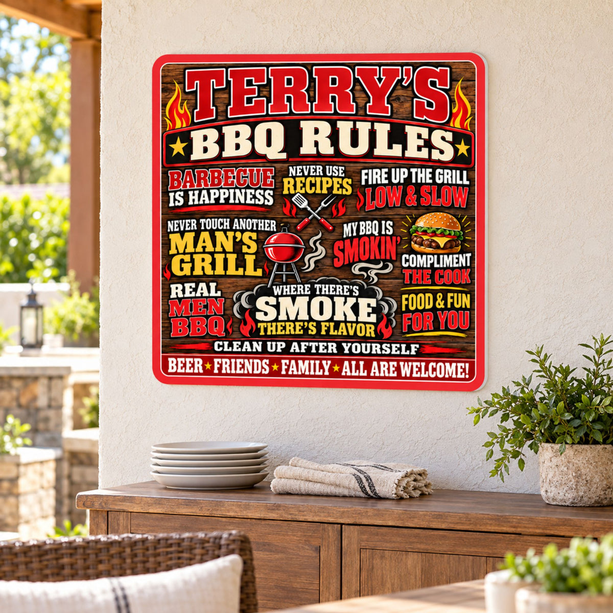 Custom BBQ Rules sign mounted on a covered patio wall above a wooden cabinet with plates and greenery.