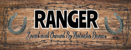 Personalized horse stall sign with a rustic brown weathered wood background, barbed wire accents, and custom text. Features the horse's name in a bold Western-style font and "Loved and Owned By" in an elegant script.