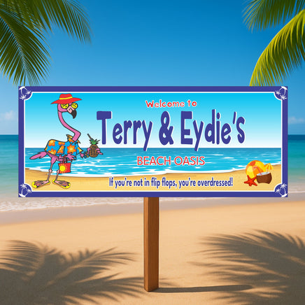 Personalized beach oasis sign with flamingo holding a drink, displayed on the sand with ocean and palm trees in the background.