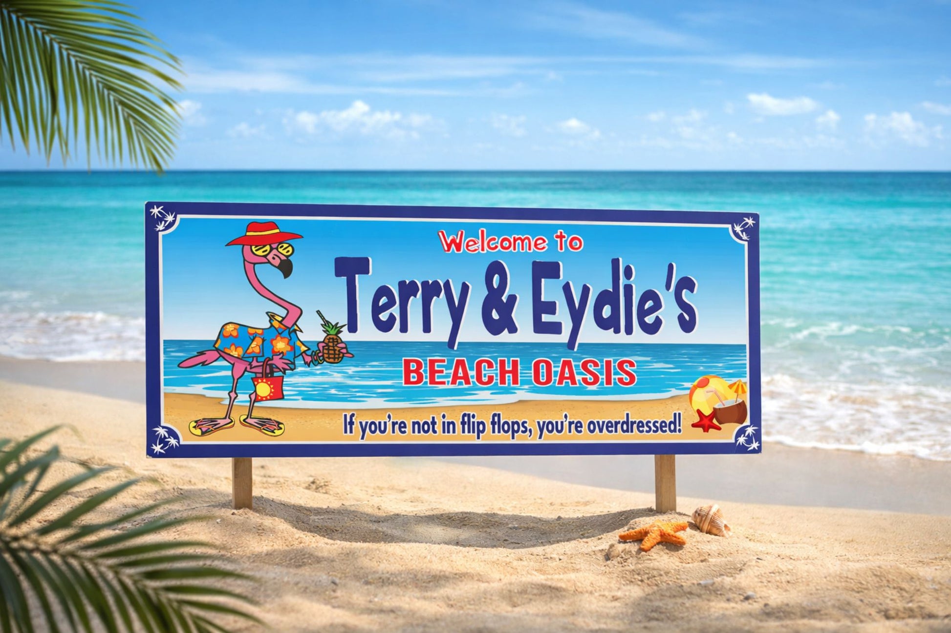 personalized flamingo beach bar sign with tropical ocean background displayed in sand on a sunny beach with palm leaves and seashells