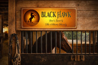 Horse stall with personalized Black Hawk sign mounted on a wooden barn wall, horse standing behind stall bars.