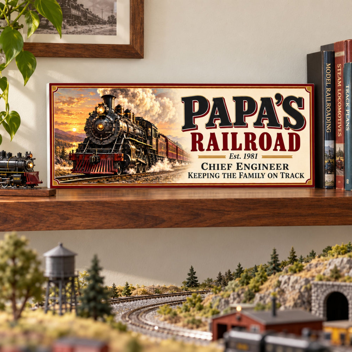 Custom railroad sign displayed on a wooden shelf beside books and a miniature locomotive, above a model railway layout.