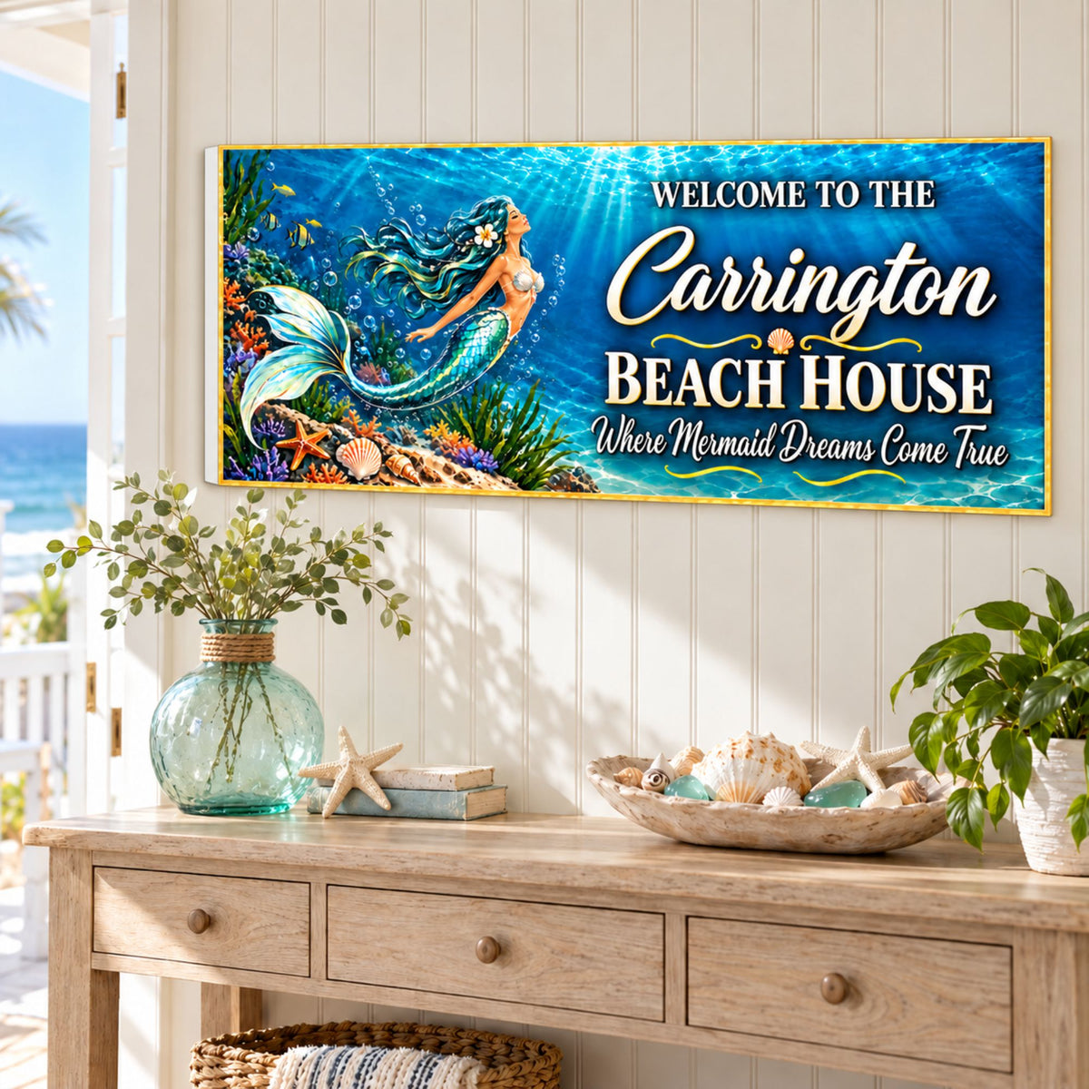 Personalized mermaid beach house sign mounted above a coastal console table with a glass vase, shells, and greenery.