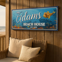 Ocean themed personalized beach house sign hanging on a porch wall above a wicker chair and pillows