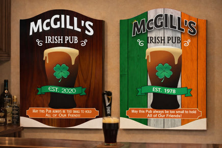 two personalized irish pub signs hanging above a home bar, one with dark wood background and one with irish flag design, each featuring pint glass and shamrock