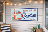 Personalized Welcome to the Lake sign mounted on an outdoor porch wall with string lights, showing oars, lifebuoy, and seagull in a coastal lake house setting