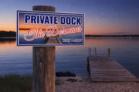 Personalized private dock sign mounted on a wooden post beside a lake at sunset, with a sandy shore and pier leading over calm water, customizable family name and message