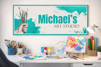 custom art studio wall sign displayed above an artist’s desk with paintbrushes, watercolor paintings, and art supplies