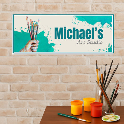art studio sign mounted on brick wall above table with paint cups and brushes