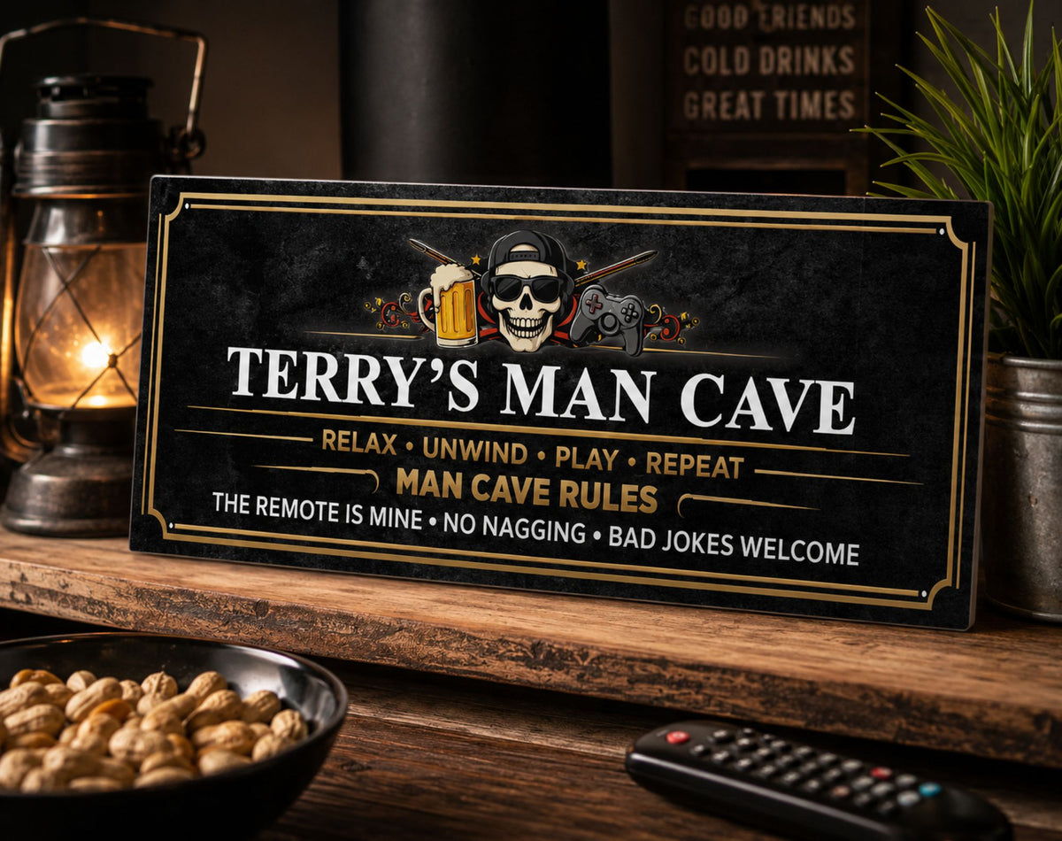 Black and gold personalized man cave sign featuring a skull, beer mug, and gaming controller, displayed on a rustic wooden shelf beside a glowing lantern and potted plant.