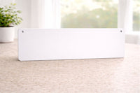 back view of rectangular aluminum sign with rounded corners and mounting holes in the top corners, resting on a tabletop indoors