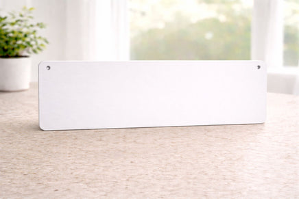 back view of rectangular aluminum sign with rounded corners and mounting holes in the top corners, resting on a tabletop indoors