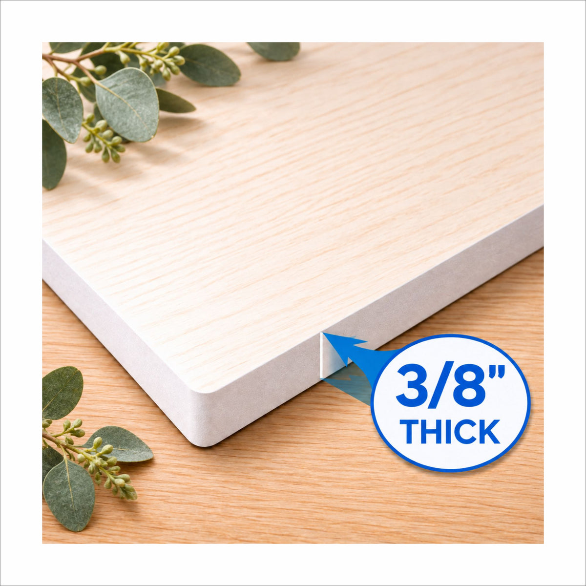 Close-up of a white KomaCel PVC sign edge on a wooden surface with eucalyptus greenery. A blue arrow and circular label indicate the sign is 3/8 inch thick