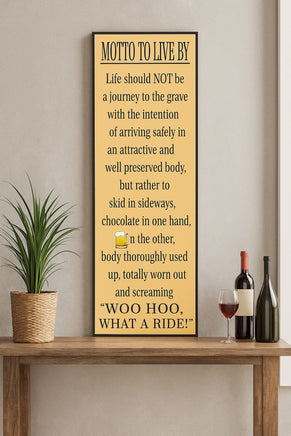 Vertical “Motto to Live By” wall sign displayed on a wooden shelf with a plant and wine bottles, humorous quote about living life to the fullest.