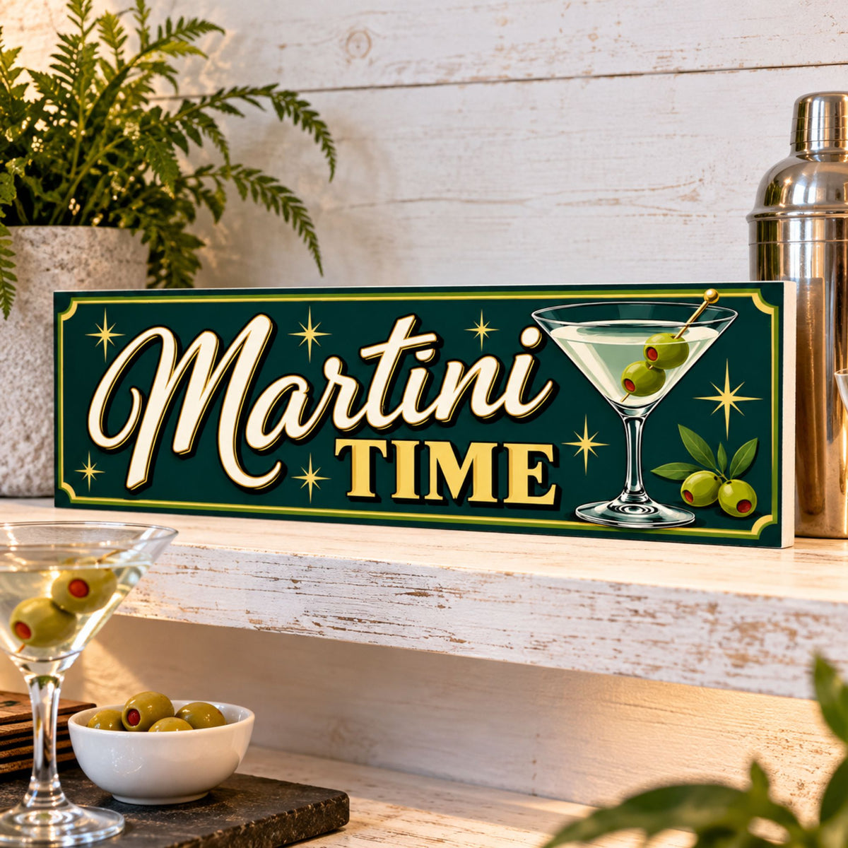 Martini Time sign displayed on a bright whitewashed bar shelf with martini glass, olives and cocktail accessories.