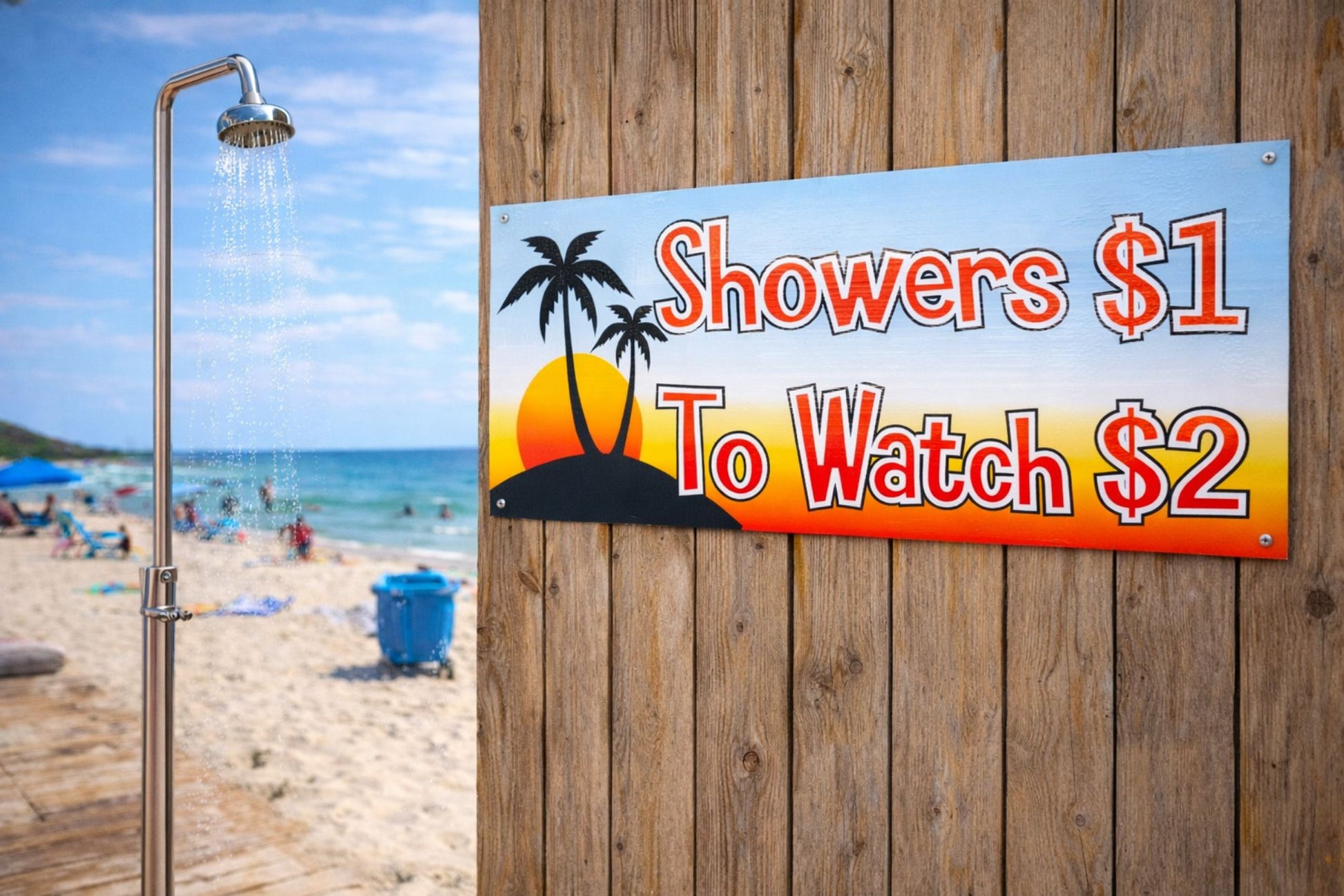 Beach shower scene with a funny Showers $1 To Watch $2 sign mounted on a wooden wall near the ocean