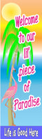 Welcome to our lil piece of paradise vertical tropical sign with palm tree, pink flamingo, bright sunset sky, and coastal phrase Life Is Good Here, printed on durable vinyl mounted to rigid PVC for indoor or outdoor display