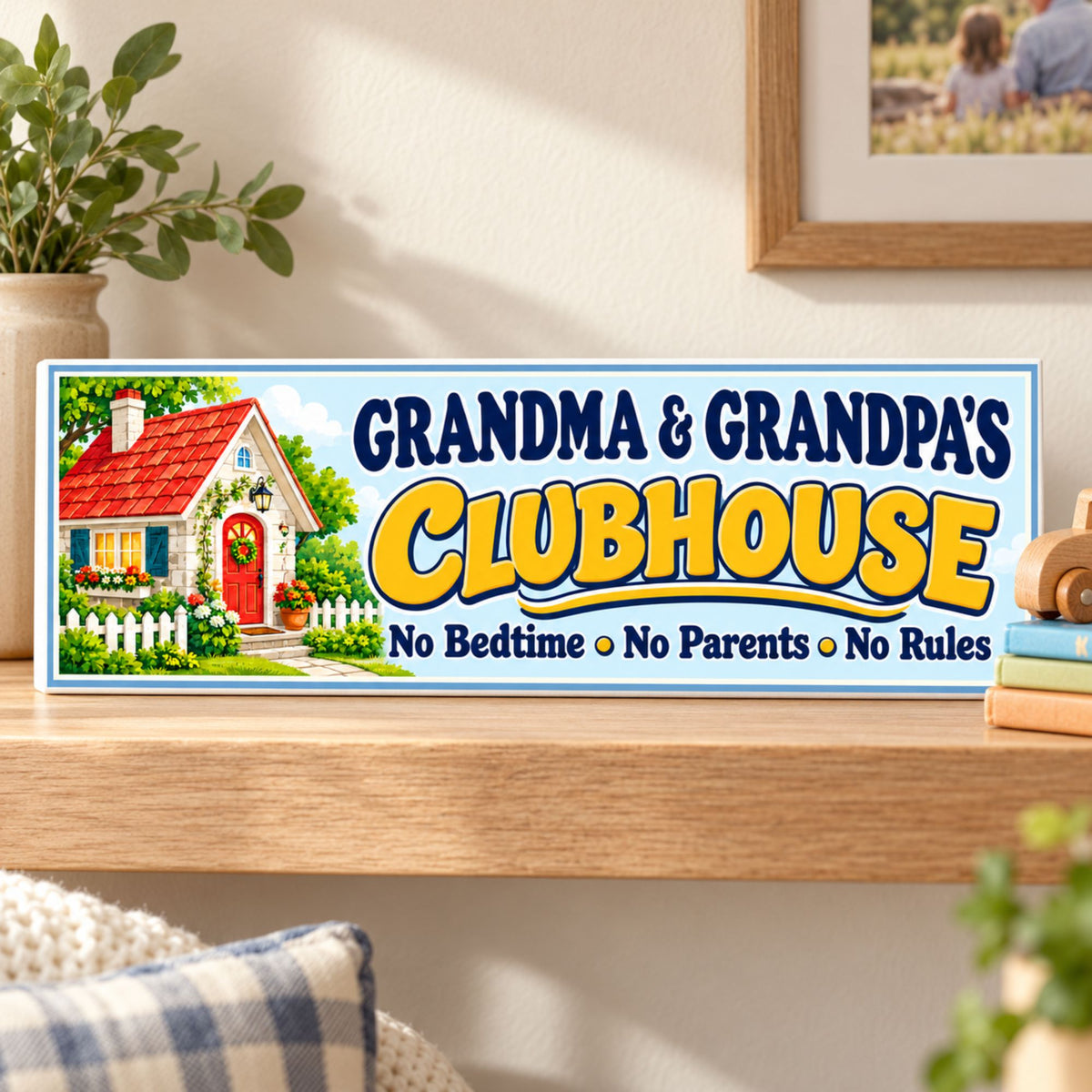 Personalized grandparents clubhouse sign with a cottage illustration, pale blue background, and yellow lettering, displayed on a wooden shelf beside books and a toy car.