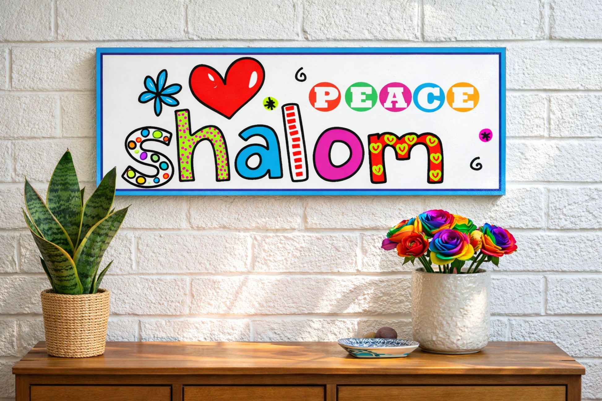 Colorful Shalom peace wall sign displayed above wooden console table with plants and flowers in bright home setting