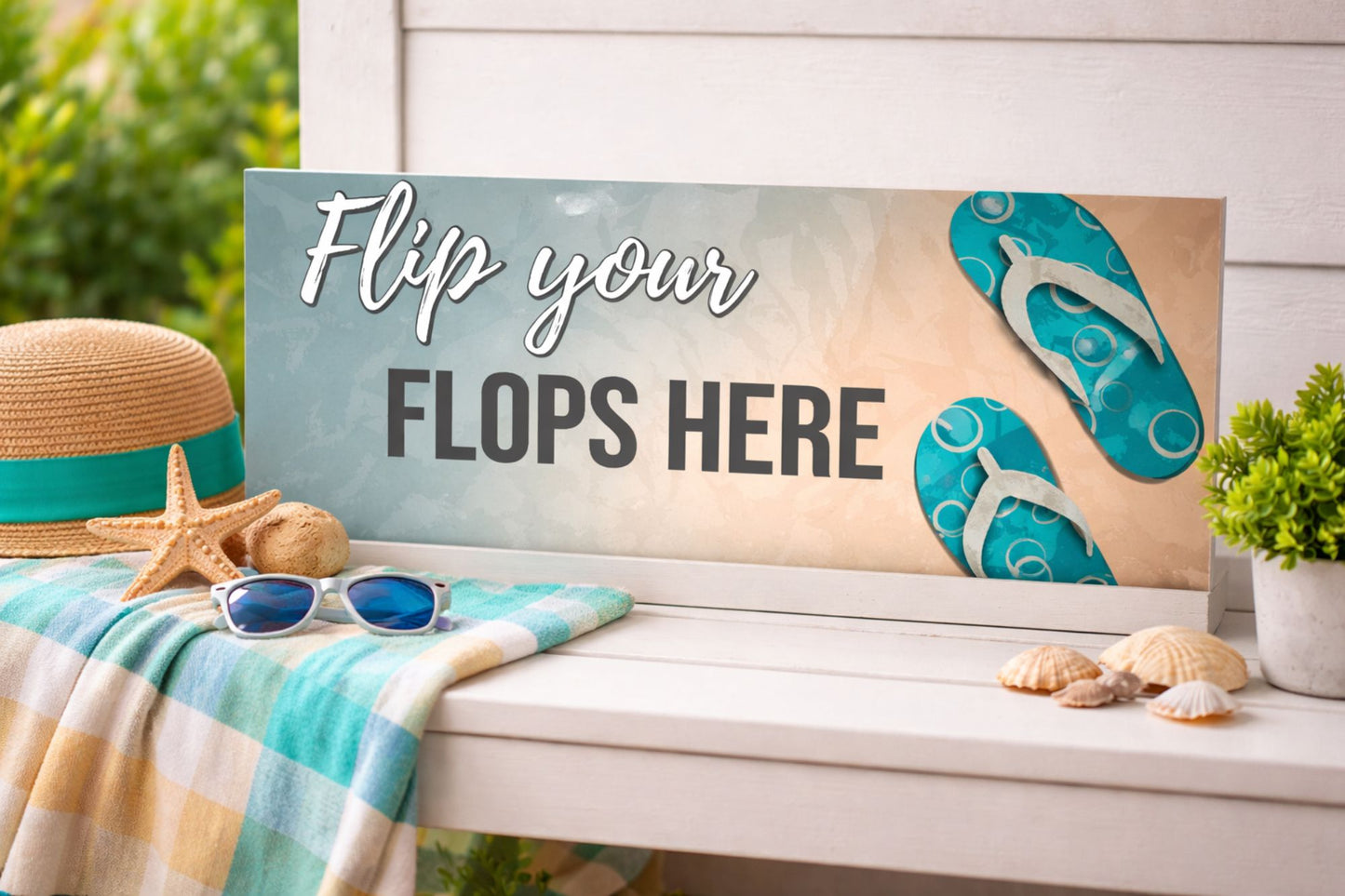 Flip your flops here beach sign displayed on white bench with coastal decor towel hat seashells and sunglasses