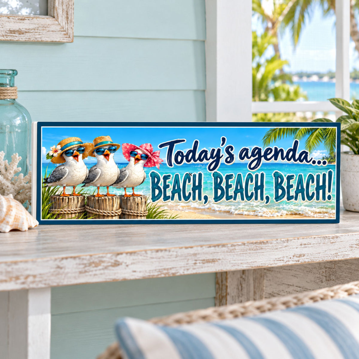 Colorful seagull beach sign displayed on a weathered white shelf in a coastal porch with pale aqua walls, seashells, and a water view.
