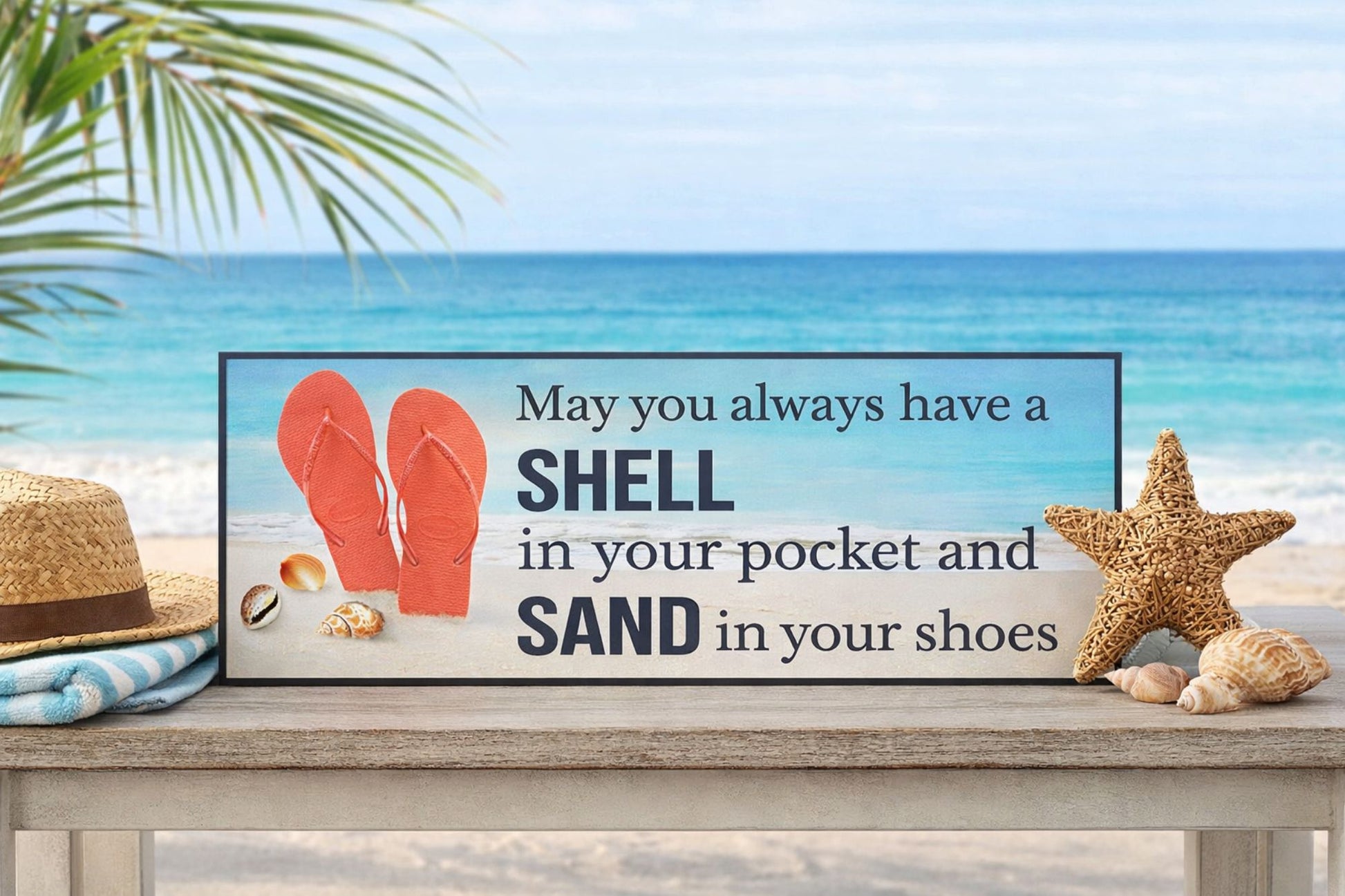 coastal beach sign reading may you always have a shell in your pocket and sand in your shoes displayed on a wooden table with ocean background, flip flops and seashell decor