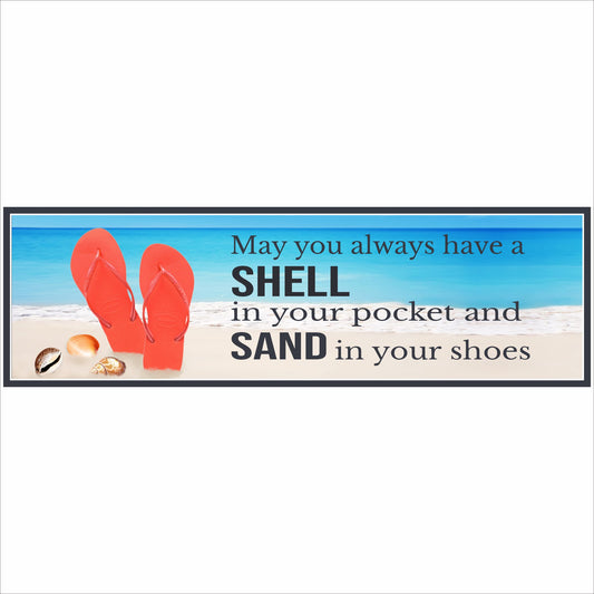 close up of coastal beach sign with flip flops and seashells reading may you always have a shell in your pocket and sand in your shoes on a wood table with ocean background