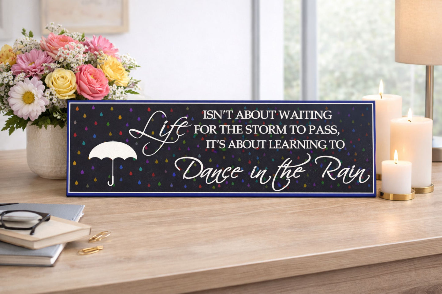lifestyle image of inspirational dance in the rain sign displayed on desk with flowers candles and cozy home decor
