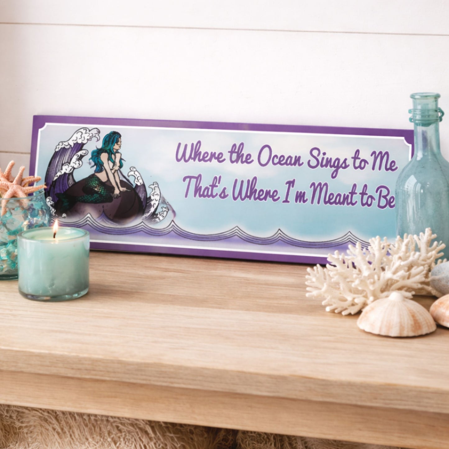 mermaid sign on a wooden surface with candles and bottles.