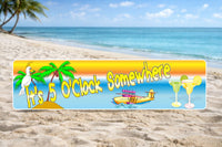 It’s 5 O’Clock Somewhere tropical sign displayed on a sandy beach with ocean and palm trees in the background