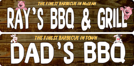 Two personalized barbecue signs displayed on rustic wood — one with pig graphics reading “Ray’s BBQ & Grill,” and one with cow graphics reading “Dad’s BBQ,” showing the available animal graphic options.