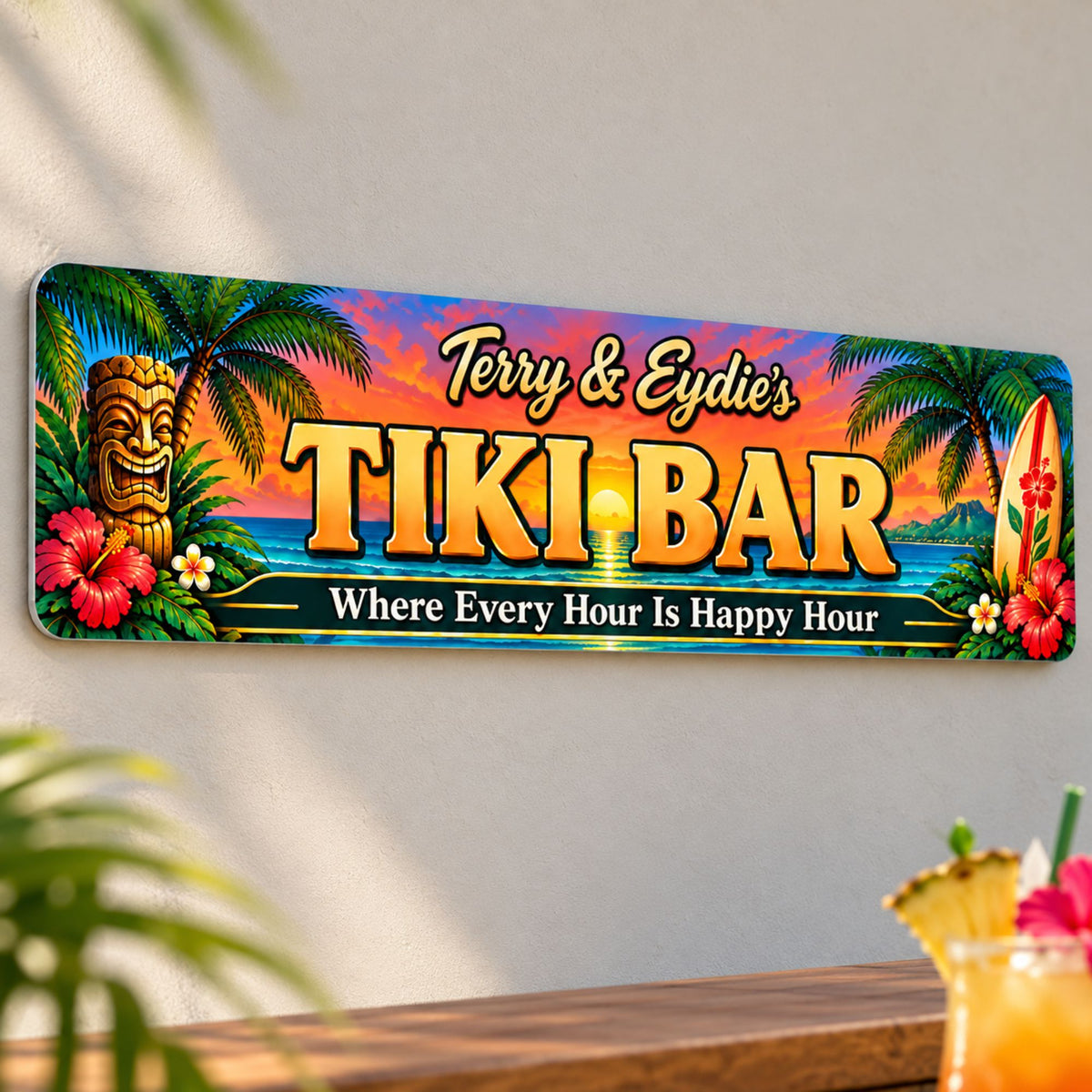 Personalized tiki bar aluminum sign mounted on a light outdoor bar wall, photographed close up with tropical greenery and a drink nearby.
