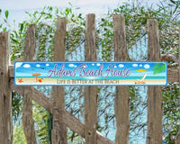Personalized aluminum beach sign featuring an illustration of a beach with an ocean backdrop, beach chair and umbrella, sea shells, and a beach ball